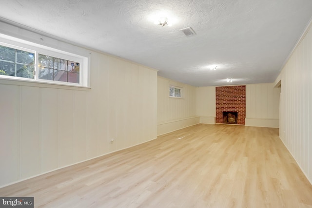 basement with a fireplace, light wood-style flooring, and a textured ceiling