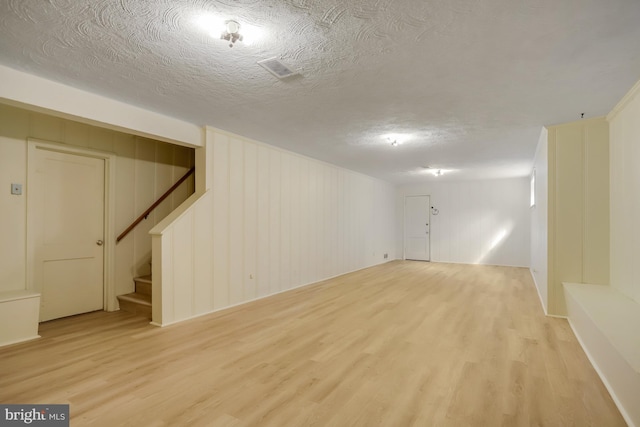 finished basement with stairway, light wood-style flooring, a textured ceiling, and visible vents