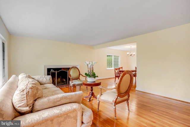 living room featuring baseboards, a fireplace with flush hearth, light wood-type flooring, and an inviting chandelier
