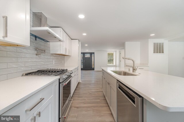 kitchen with light wood-type flooring, a sink, backsplash, stainless steel appliances, and wall chimney exhaust hood