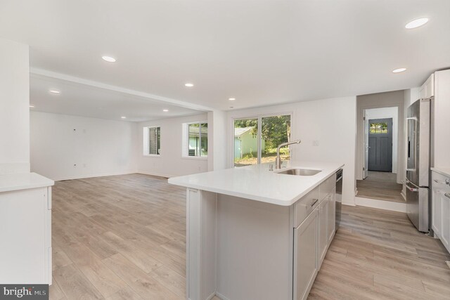 kitchen with a center island with sink, light wood finished floors, a sink, light countertops, and appliances with stainless steel finishes