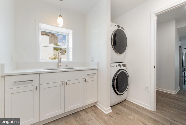 clothes washing area with stacked washer and dryer, light wood-style floors, baseboards, and a sink