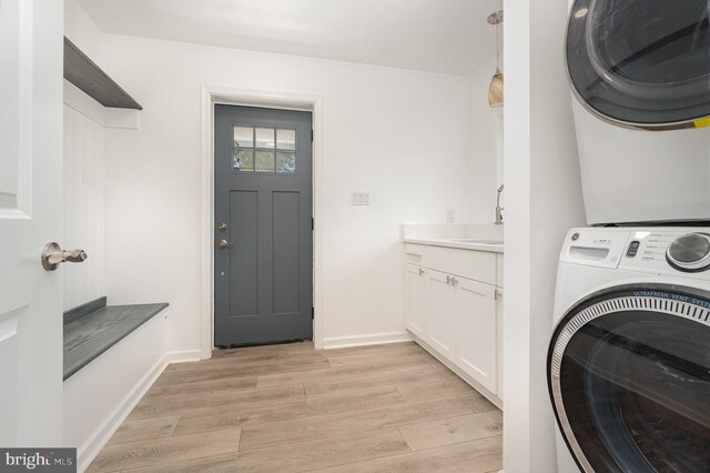 laundry room with a sink, cabinet space, light wood-style floors, and stacked washer and dryer