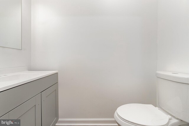 half bathroom with baseboards, toilet, and vanity