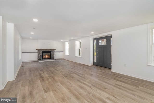 unfurnished living room featuring recessed lighting, baseboards, a stone fireplace, and light wood finished floors