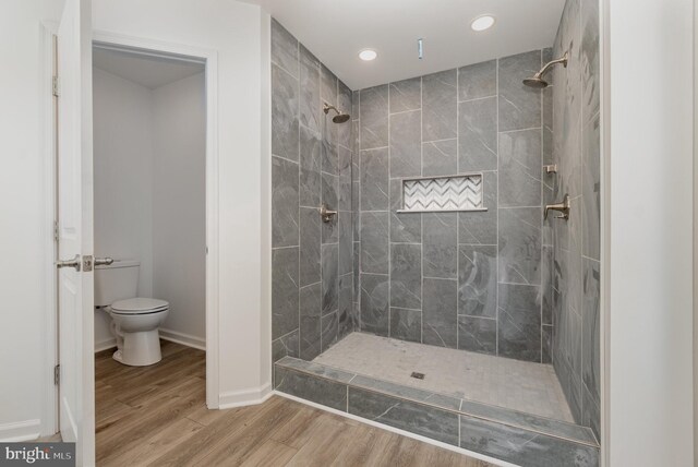 full bathroom featuring baseboards, tiled shower, toilet, and wood finished floors