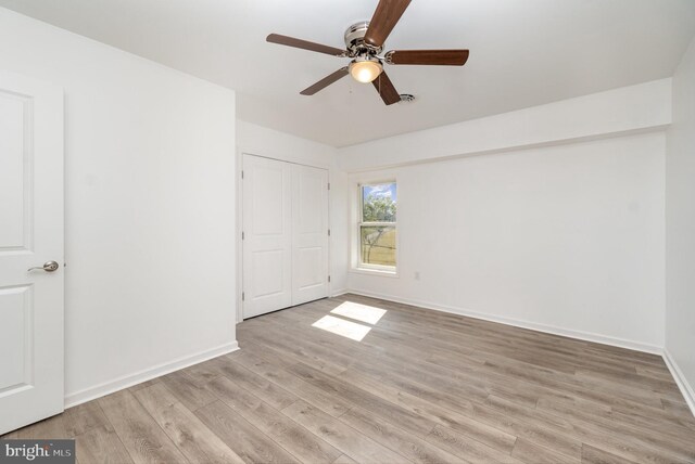 unfurnished bedroom featuring light wood-style flooring, a ceiling fan, baseboards, and a closet