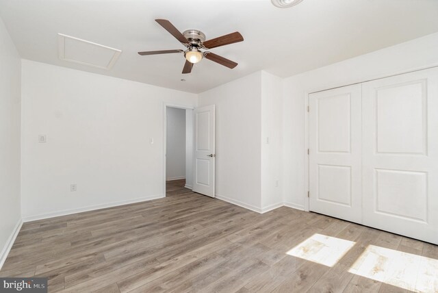 unfurnished bedroom with a closet, light wood finished floors, baseboards, attic access, and ceiling fan