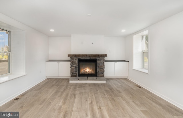 unfurnished living room featuring a stone fireplace, wood finished floors, and baseboards