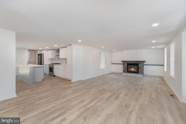 unfurnished living room with recessed lighting, a fireplace, baseboards, and light wood-style floors