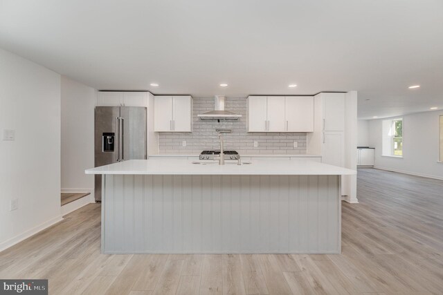 kitchen featuring an island with sink, high end refrigerator, light countertops, and wall chimney exhaust hood