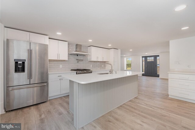 kitchen featuring light countertops, light wood-style floors, stainless steel refrigerator with ice dispenser, wall chimney exhaust hood, and a sink