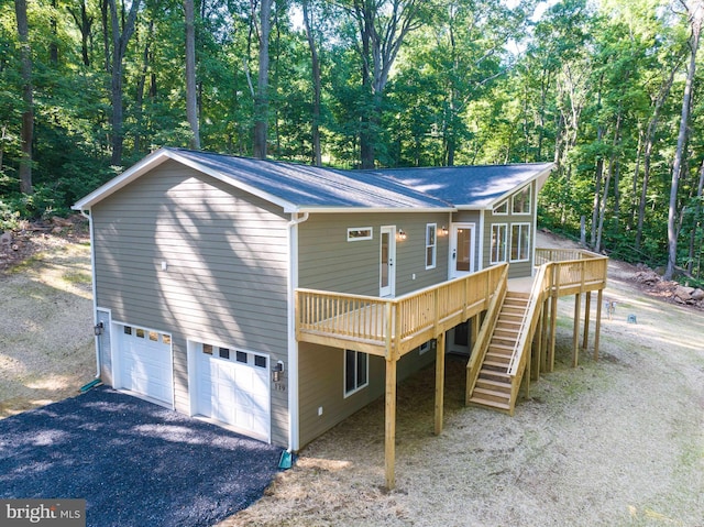 view of front of home with a wooden deck, a garage, driveway, a forest view, and stairs