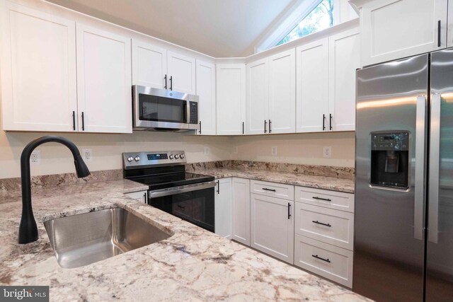 kitchen with vaulted ceiling, white cabinetry, stainless steel appliances, and sink