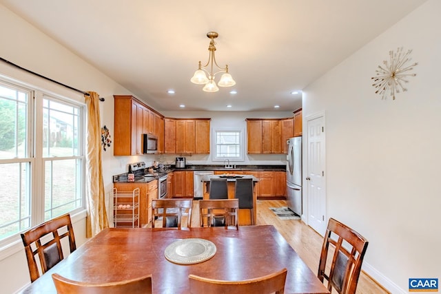 dining space with a healthy amount of sunlight, an inviting chandelier, sink, and light wood-type flooring