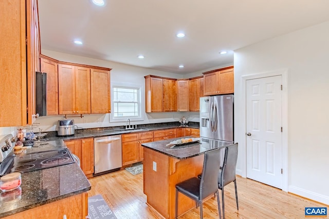 kitchen featuring appliances with stainless steel finishes, a center island, sink, light wood-type flooring, and dark stone counters