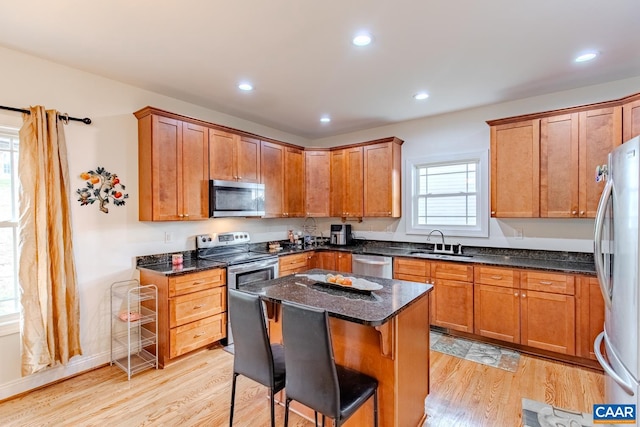 kitchen featuring a kitchen island, light hardwood / wood-style flooring, appliances with stainless steel finishes, sink, and dark stone countertops