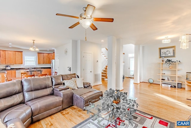 living room with ceiling fan with notable chandelier and light hardwood / wood-style floors