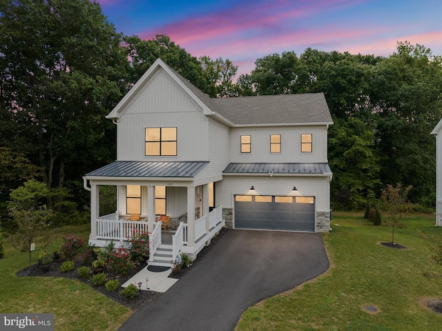 modern farmhouse with a porch, aphalt driveway, an attached garage, stone siding, and a standing seam roof