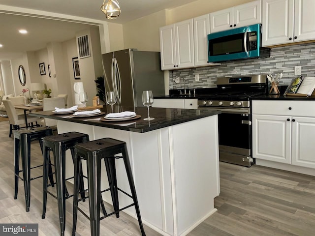 kitchen with white cabinets, light hardwood / wood-style floors, appliances with stainless steel finishes, and a kitchen island