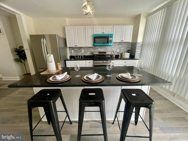 kitchen with appliances with stainless steel finishes, light wood-type flooring, white cabinetry, and a kitchen breakfast bar