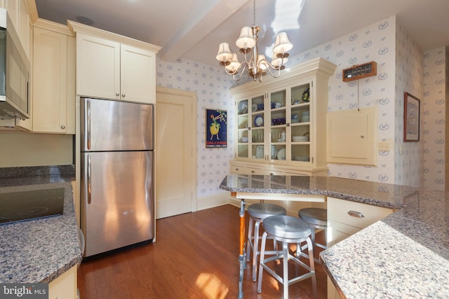 kitchen featuring cream cabinets, appliances with stainless steel finishes, dark hardwood / wood-style flooring, beamed ceiling, and a breakfast bar