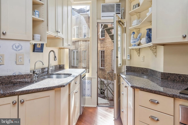 kitchen featuring dark stone counters, wood-type flooring, sink, cream cabinets, and an AC wall unit