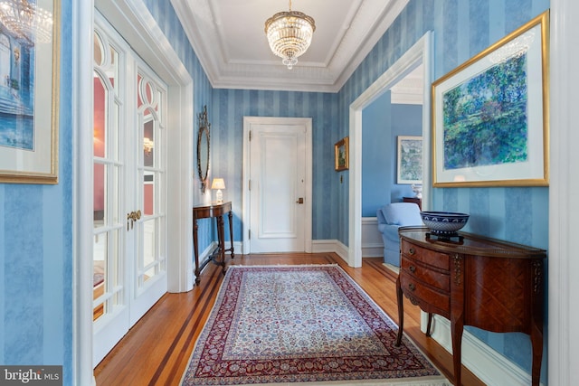 doorway with wallpapered walls, ornamental molding, a notable chandelier, and wood finished floors