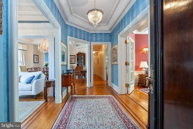 interior space with a chandelier, crown molding, wood finished floors, and wallpapered walls