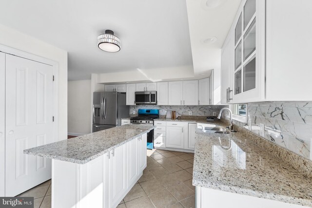 kitchen with light stone countertops, tasteful backsplash, stainless steel appliances, sink, and white cabinets