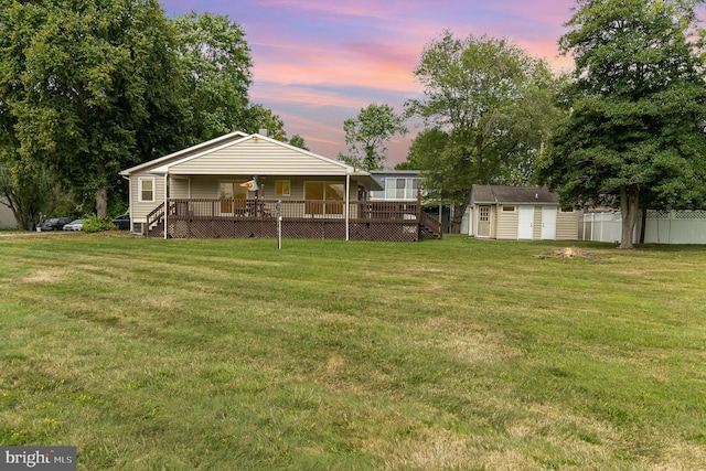 back of property featuring a wooden deck, a lawn, a storage unit, fence, and an outdoor structure