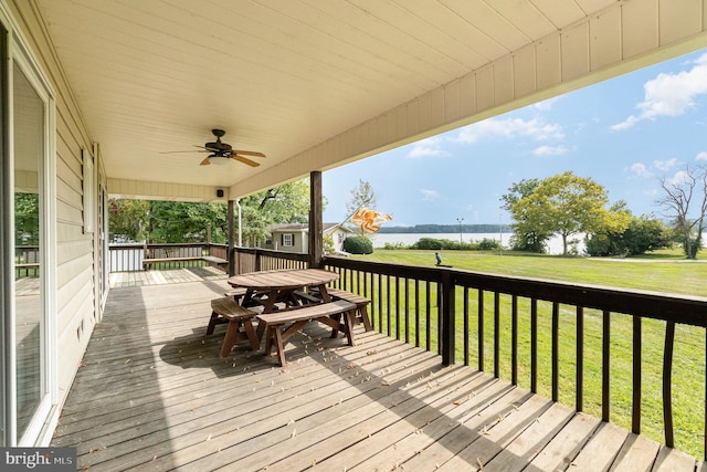 wooden terrace featuring outdoor dining area, a water view, a lawn, and ceiling fan