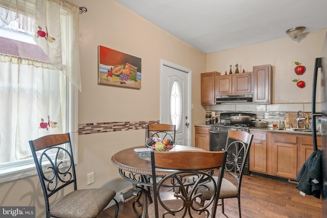 kitchen with under cabinet range hood, wood finished floors, a sink, backsplash, and gas range oven