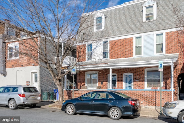 view of front of property featuring brick siding, roof with shingles, and mansard roof