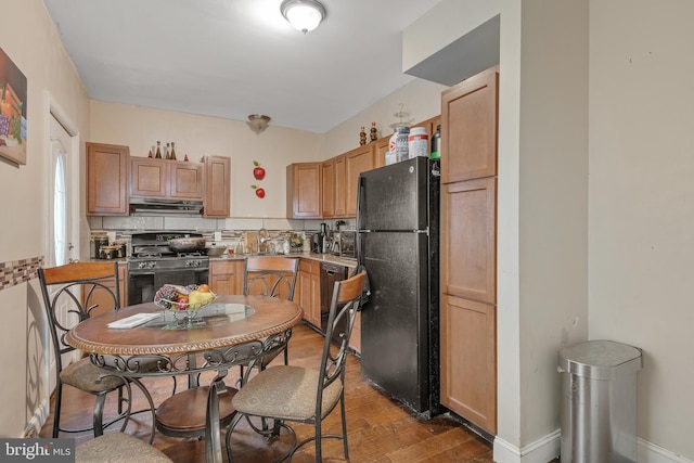 kitchen featuring baseboards, decorative backsplash, wood finished floors, under cabinet range hood, and black appliances