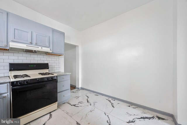 kitchen featuring marble finish floor, decorative backsplash, gas range, under cabinet range hood, and baseboards