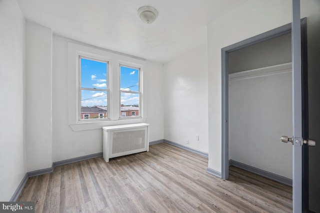 unfurnished bedroom featuring radiator heating unit, a closet, baseboards, and wood finished floors