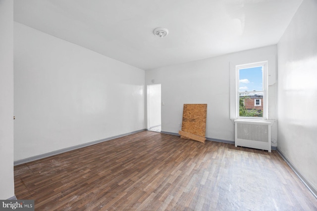 unfurnished room featuring radiator heating unit, wood finished floors, and baseboards