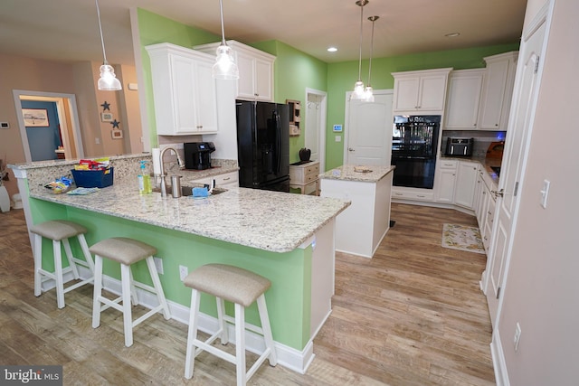 kitchen featuring a breakfast bar area, black appliances, kitchen peninsula, sink, and light wood-type flooring