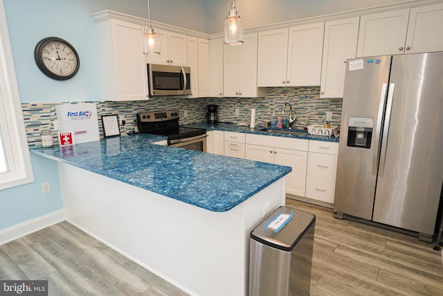 kitchen featuring light hardwood / wood-style flooring, hanging light fixtures, stainless steel appliances, sink, and kitchen peninsula