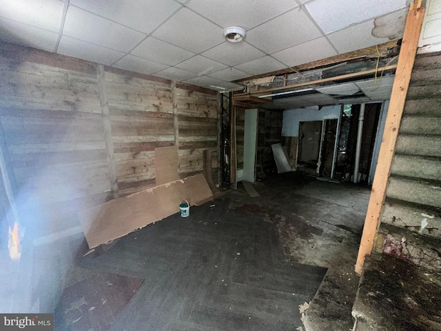 basement with wood walls and a drop ceiling