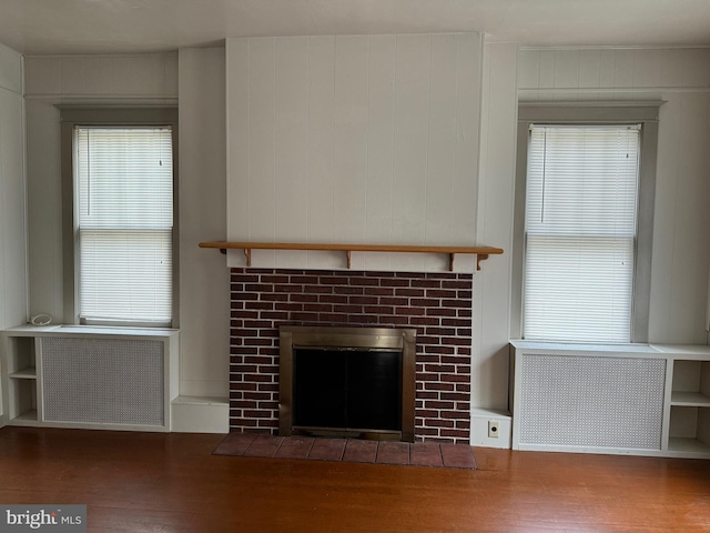 unfurnished living room featuring radiator, wooden walls, hardwood / wood-style flooring, and a fireplace