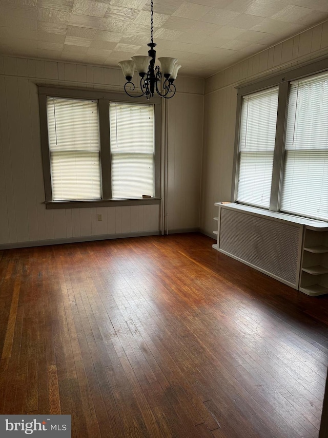 empty room with radiator, dark hardwood / wood-style floors, and a notable chandelier