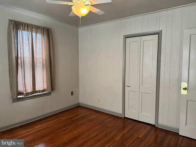 unfurnished bedroom with wooden walls, dark hardwood / wood-style flooring, a closet, ceiling fan, and ornamental molding