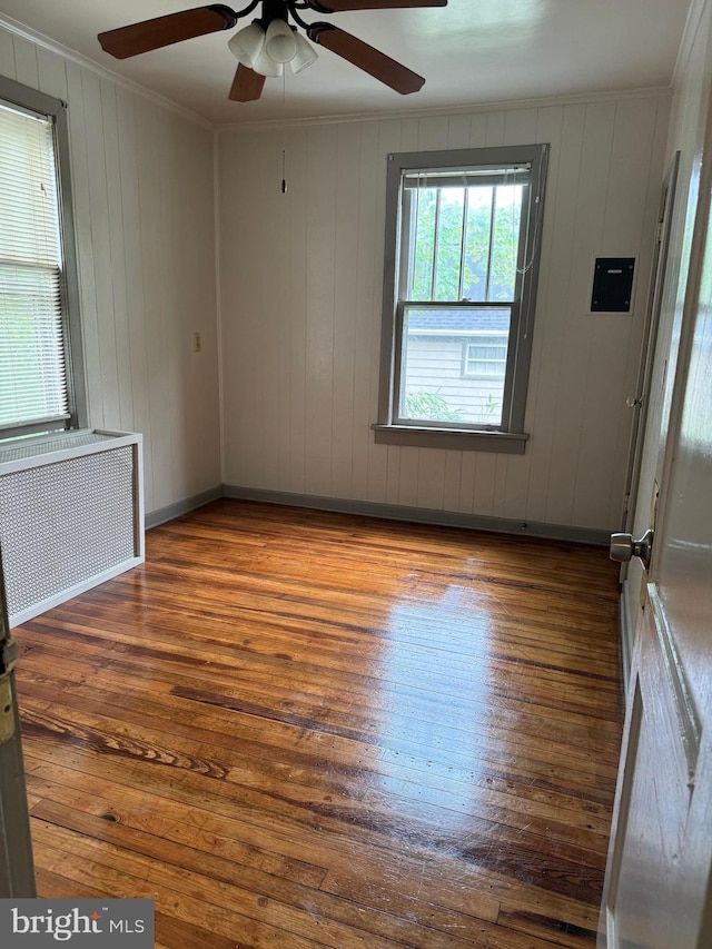 empty room featuring ceiling fan, hardwood / wood-style flooring, radiator heating unit, and crown molding