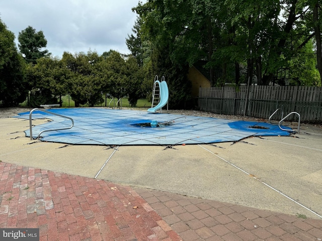 view of swimming pool with a water slide, a patio area, and a diving board