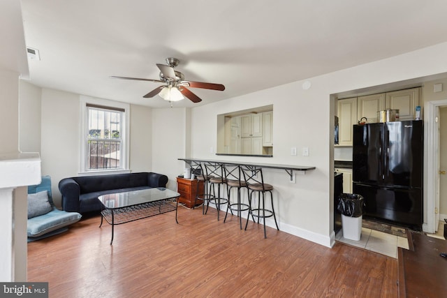 living room featuring ceiling fan, wood finished floors, visible vents, and baseboards