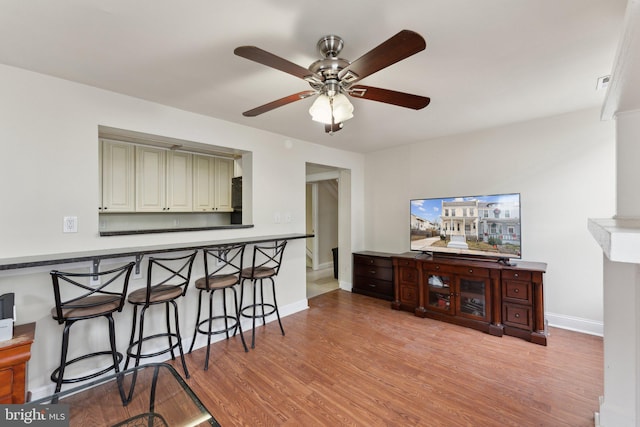 kitchen featuring a breakfast bar, ceiling fan, baseboards, and wood finished floors