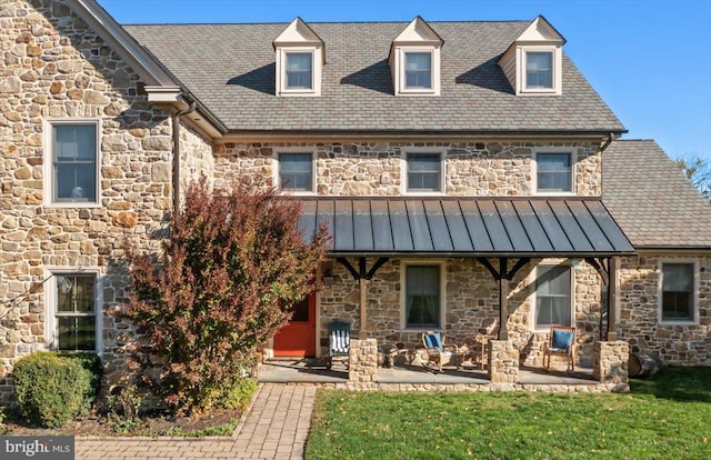 view of front of property featuring a patio, a standing seam roof, metal roof, a high end roof, and stone siding