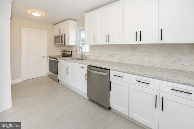 kitchen with white cabinets, backsplash, appliances with stainless steel finishes, light stone counters, and sink